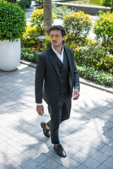 Successful man in formal black suit and sunglasses walking on the street and looking aside. High quality photo