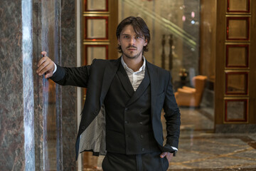 Portrait of handsome young business man wearing black classic suit standing near modern building....