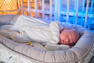 Portrait of a baby boy aged one month sleeping in a crib. Caucasian child in the childrens bedroom