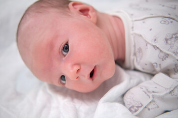 A baby aged 1 month learns to keep his head lying on his stomach. Caucasian boy child in a home white bedroom