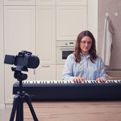 A woman in a blue shirt records piano lessons on a video camera. Learning music in the home kitchen