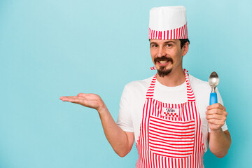 Young caucasian maker holding a scoop isolated on blue background showing a copy space on a palm and holding another hand on waist.