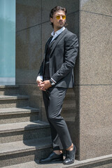 Handsome man in black formal suit and yellow sunglasses standing on the stairs. High quality photo