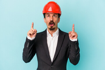 Young architect caucasian man isolated on blue background pointing upside with opened mouth.
