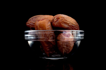 Several dried organic dates in a glass bowl, close-up, isolated on black.