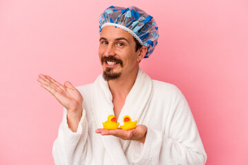 Young caucasian man going to the shower with rubber ducks isolated on pink background showing a...