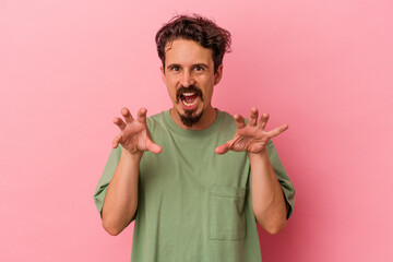 Young caucasian man isolated on pink background showing claws imitating a cat, aggressive gesture.