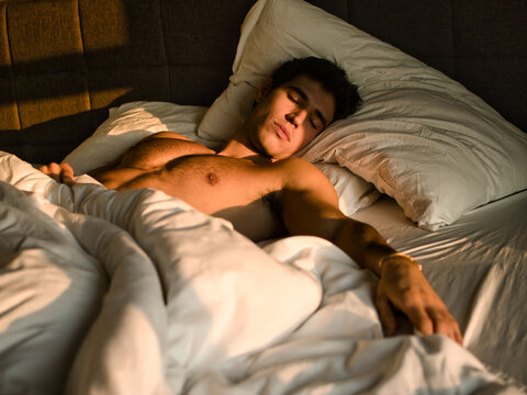 Handsome shirtless young man in bed sleeping