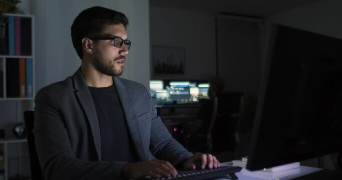 Focused caucasian businessman working on desktop computer at office. Male professional typing on keyboard at night. Portrait of positive brunette bearded millennial business man looking at screen.