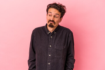 Fototapeta premium Young caucasian man isolated on pink background shrugs shoulders and open eyes confused.
