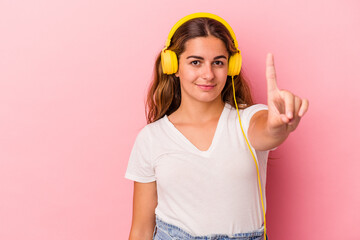 Young caucasian woman listening to music isolated on pink background  showing number one with finger.