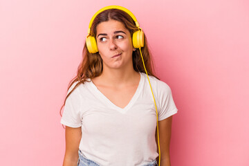 Young caucasian woman listening to music isolated on pink background  confused, feels doubtful and unsure.