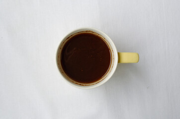 Gently yellow with white mug with fragrant invigorating morning coffee on a white background top view