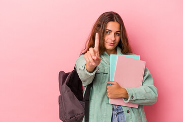 Fototapeta premium Young caucasian student woman holding books isolated on pink background showing number one with finger.