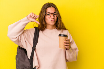 Young caucasian student woman holding coffee isolated on yellow background  showing a dislike gesture, thumbs down. Disagreement concept.