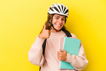Young caucasian student woman wearing a bike helmet isolated on yellow background  smiling and raising thumb up