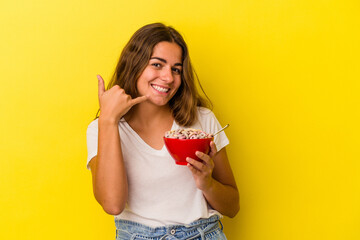 Young caucasian woman holding cereals isolated on yellow background  showing a mobile phone call gesture with fingers.