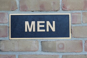 A close view of the metal men sign on the brick wall.