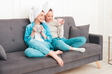 Two young beautiful smiling women.Sexy carefree models sitting on bed in posh apartment.They doing beauty treatments at home in towels on heads. Drinking tea or coffee, holding cup