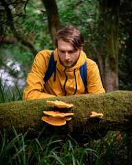 Man in a yellow jacket looking at mushrooms on a fallen tree