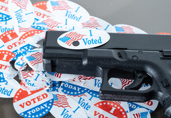 Concept for election violence with handgun decorated with I voted today sticker with hole made by...