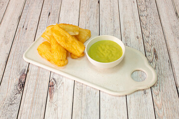 Tray of delicious fried yucca with green sauce to dip in a small white bowl