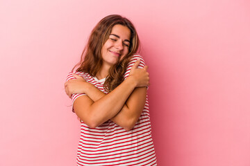 Young caucasian woman isolated on pink background  hugs, smiling carefree and happy.