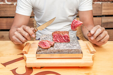 Beef sirloin cooked on the boiling stone with the point of doneness chopped by the hands of a man on a wooden table