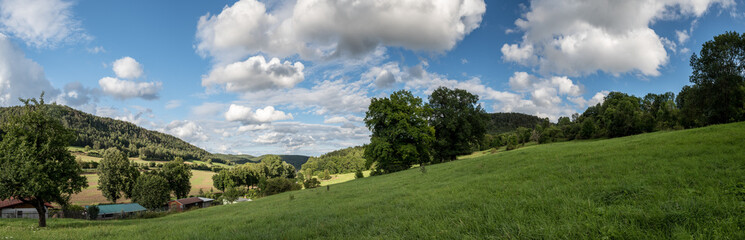 Tal in Thüringer Mittelgebirge mit Häusern, Bäumen uns Weisen , Wolken und blauem Himmel im...