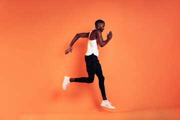 Fototapeta na wymiar Male athlete wearing sports clothes running against an orange background