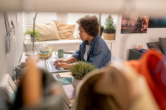 Cute teenage girl typing on laptop keypad while carrying out homework in bedroom