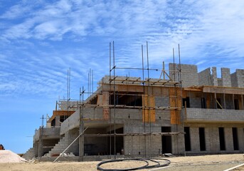 Low angle view towards a building construction site with scaffolding and block material, and blue sky in the background