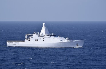 White ocean going patrol vessel equipped with sophisticated communications equipment in the dark blue ocean with blue sky in the background