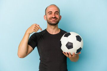 Young business bald man playing football isolated on blue background  person pointing by hand to a shirt copy space, proud and confident
