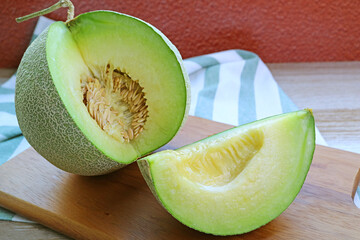 Fresh Ripe Muskmelon with a Juicy Slice Cut from Whole Fruit on Wooden Cutting Board