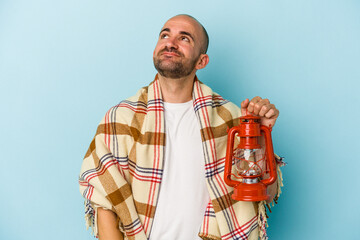 Young bald man holding vintage lantern isolated on blue background  dreaming of achieving goals and...