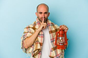 Obraz premium Young bald man holding vintage lantern isolated on blue background keeping a secret or asking for silence.