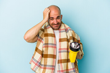 Young bald man holding vintage lantern isolated on blue background  being shocked, she has...