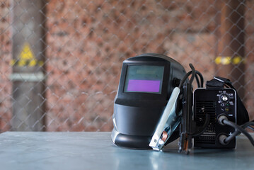 Welding inverter and welding mask on the metal workbench background. Front view.