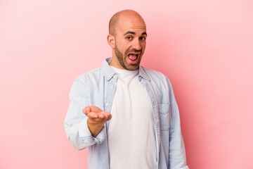 Young caucasian bald man isolated on pink background  stretching hand at camera in greeting gesture.