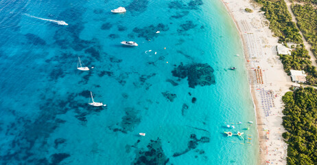 Fototapeta na wymiar View from above, stunning aerial view of a green coastline with a white sand beach and and boats sailing on a turquoise water at sunset. Cala di volpe beach, Costa Smeralda, Sardinia, Italy...