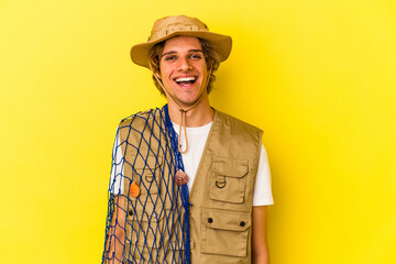 Young fisherman with makeup holding a net isolated on yellow background  happy, smiling and cheerful.