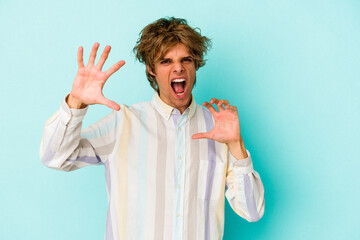 Young caucasian man with make up isolated on blue background  upset screaming with tense hands.