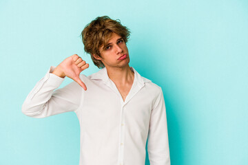 Young caucasian man with make up isolated on blue background  showing a dislike gesture, thumbs...