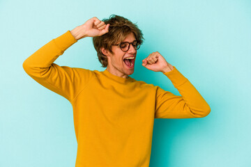 Young caucasian man with make up isolated on blue background celebrating a special day, jumps and raise arms with energy.