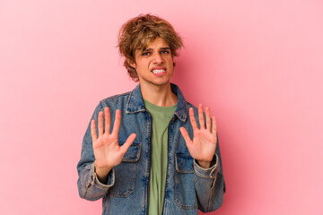 Young caucasian man with make up isolated on pink background rejecting someone showing a gesture of...