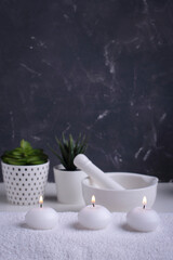 Spa background concept. Burning white candles on towel. Candles, succulent, mortar on grey wall.