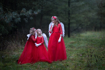 Drei Engel Mädchen mit den roten Kleidern, weißen Flügeln sehen sehr rätselhaft aus. Sie halten Zeigefinger vom Mund und bieten um leise zu sein, daß sie keiner hört, Weihnachten