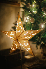 Christmas star on background of christmas tree in lights in evening room. Big paper star garland...