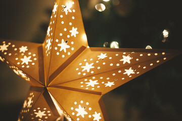 Christmas star close up on background of christmas tree in lights in evening room. Big paper star...
